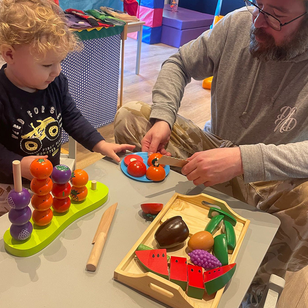 Wooden fruit and vegetable tray with VELCRO® pads, allowing children to safely cut through and reassemble the pieces using the included wooden knife. Promotes coordination skills, understanding of proportion, division, and illustrates simple fractions thr